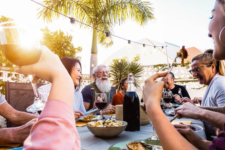 Happy family doing a dinner during sunset time outdoor - Group of diverse friends having fun dining together outside - Concept of lifestyle people, food and weekend activities